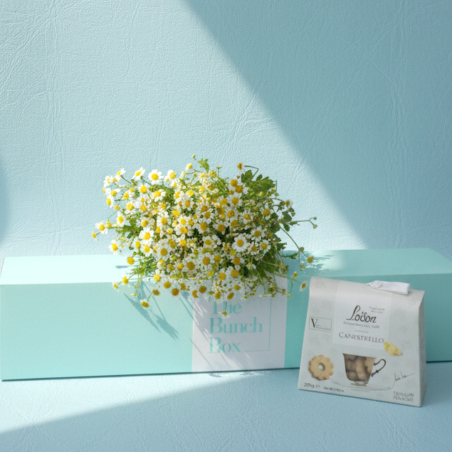 Tanacetum Daisy and Loacker Biscuit Box features ten stems of whimsical, fresh Tanacetum daisies paired with 200g of buttery Loison Canestrello biscuits. Presented in our signature mint green long-form gift box, this set offers a sophisticated yet playful gifting solution that blends rustic botanical charm with the heritage of premium Italian confectionery. It is a delightful choice for brightening someone's day with a touch of natural elegance.